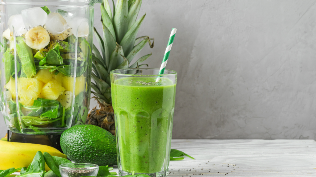 Green juice detox ingredients on wooden surface with pineapple avocado banana and leafy greens and kiwi and chia seeds
