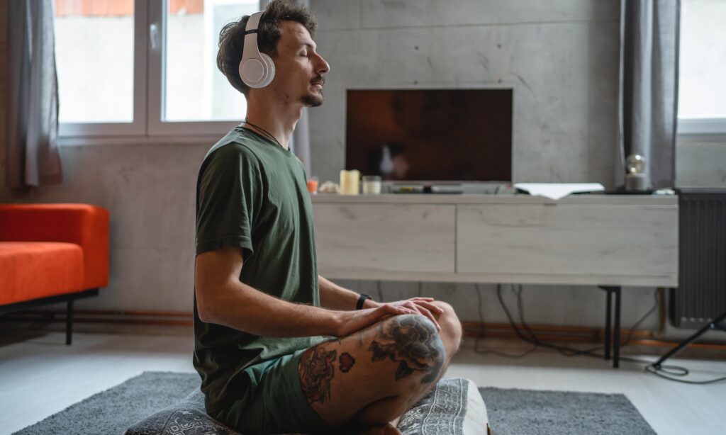 one man adult caucasian male on the floor use headphones for online guided meditation practicing mindfulness yoga with eyes closed at home real people self care manifestation concept copy space