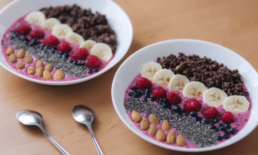 Gluten free dairy free breakfast smoothie bowl with banana berries almonds almond milk raspberry very tasty. Smoothie bowl with fresh raspberry, blueberry, chia seeds, almonds, banana, and chocolate flakes. Morning breakfast on wooden table.